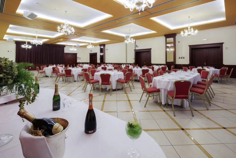 Nell'immagine, il ristorante del Classic Hotel: si vedono alcuni tavoli apparecchiati con delle sedie rosse e, in primo piano sulla sinistra, un tavolo su cui sono poggiate delle bottiglie di spumante. Dal soffitto pendono dei lampadari.