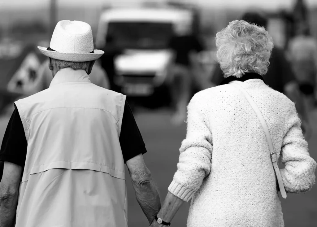 In this black and white picture, an old couple, seen from behind, walking hand in hand.